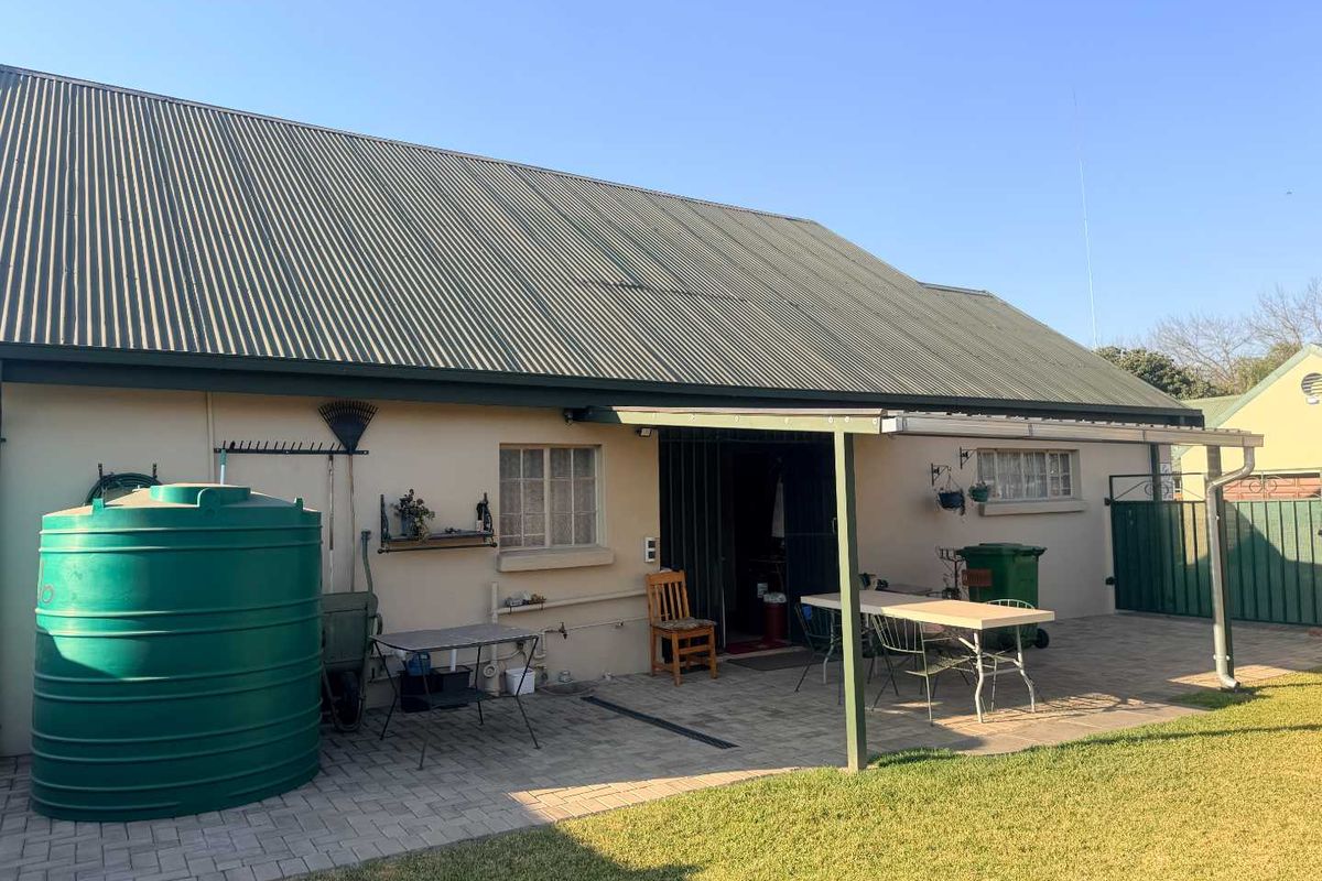 Rear view of the property featuring a paved patio area, corrugated metal roof, and a large water storage tank.