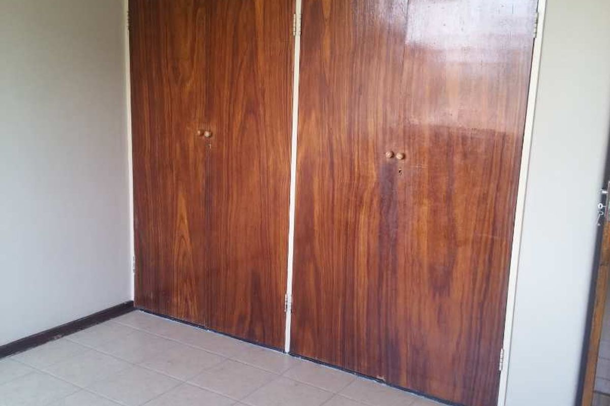 An empty bedroom featuring tiled flooring and floor-to-ceiling built-in wooden cupboards with overhead storage compartments.