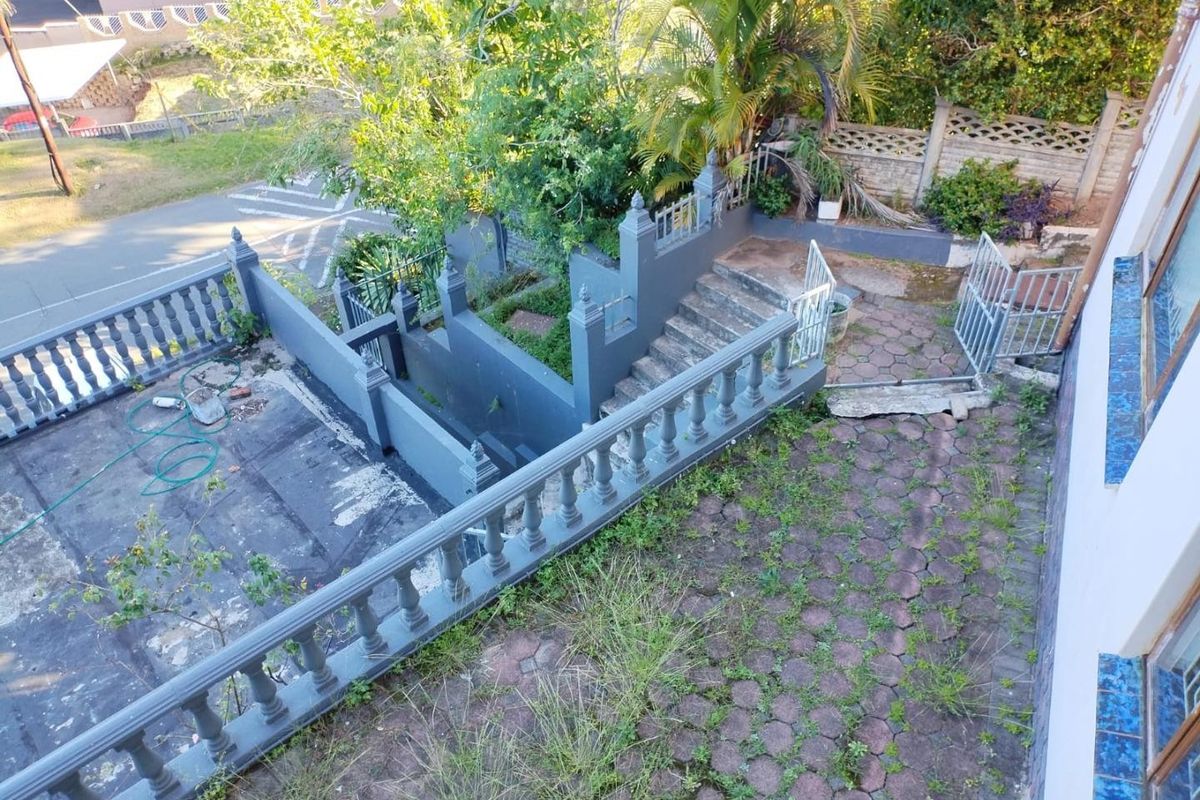 An elevated view of a rear outdoor area featuring a paved patio, concrete balustrades, and stairs leading to a lower garden level.