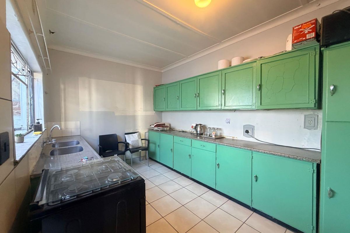 A functional kitchen featuring green built-in cabinetry, a double sink, gas stove, and tiled flooring, offering potential for modernization and cosmetic updates.