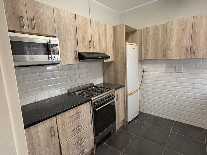 Modern kitchen featuring light wood-grain cabinetry, subway tile backsplash, dark stone countertops, and integrated stainless steel appliances.