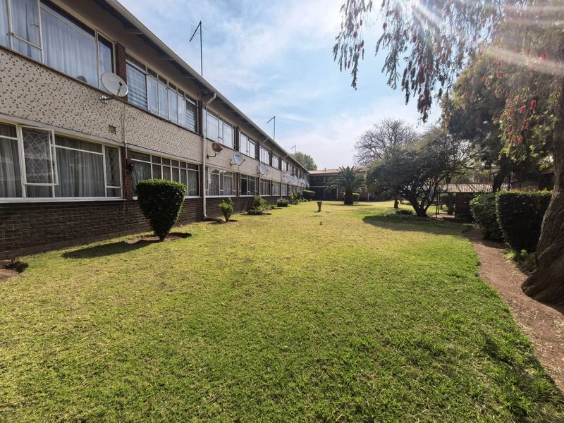 A view of the rear exterior of the apartment complex, featuring a large communal lawn area and multi-story brick building facade.