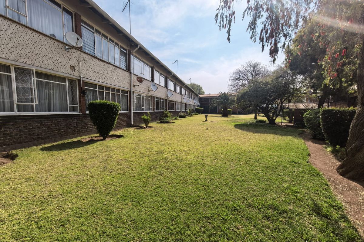 A view of the rear exterior of the apartment complex, featuring a large communal lawn area and multi-story brick building facade.