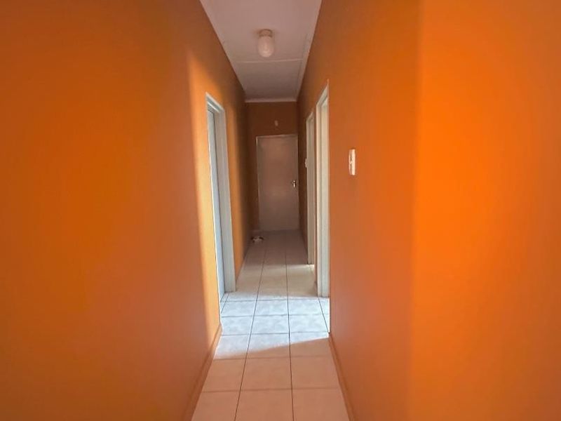A simple, empty residential hallway featuring tiled flooring and bright orange wall paint, providing access to multiple rooms.