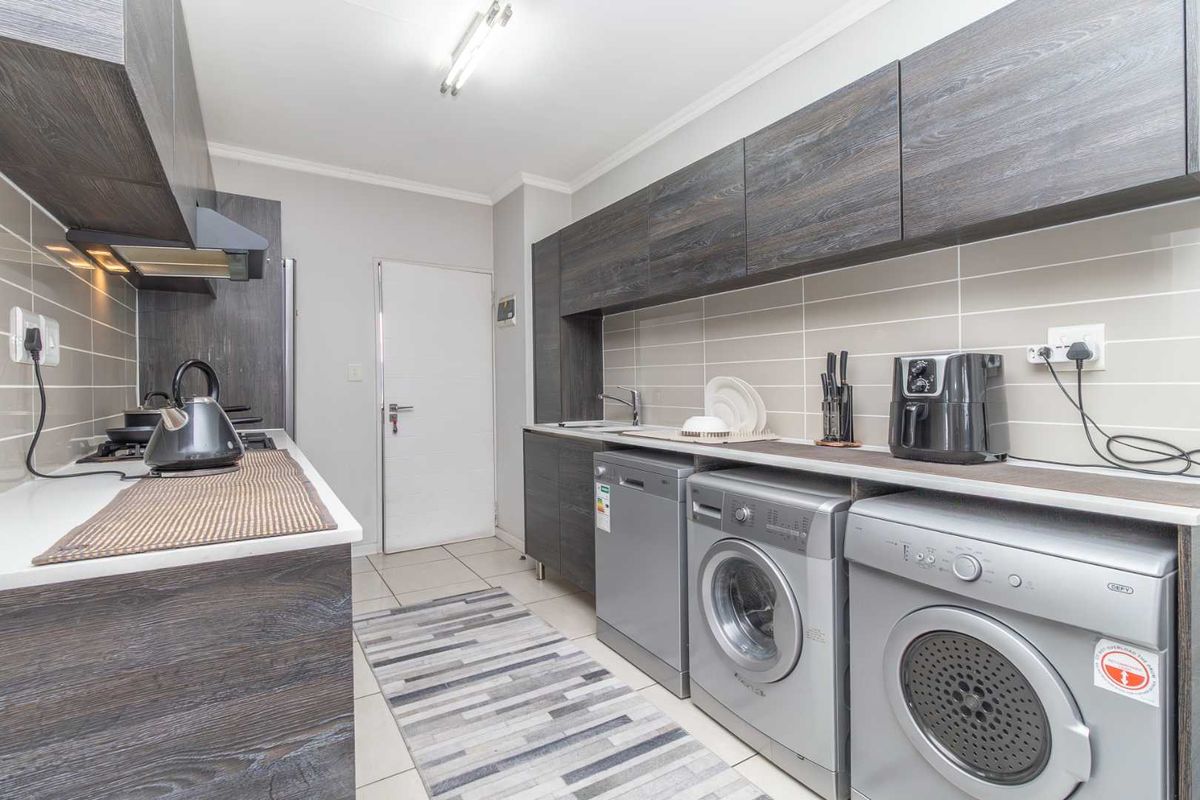 Modern kitchen featuring dark wood-grain cabinetry, tiled backsplash, integrated gas hob, extractor fan, and dedicated space for laundry appliances.