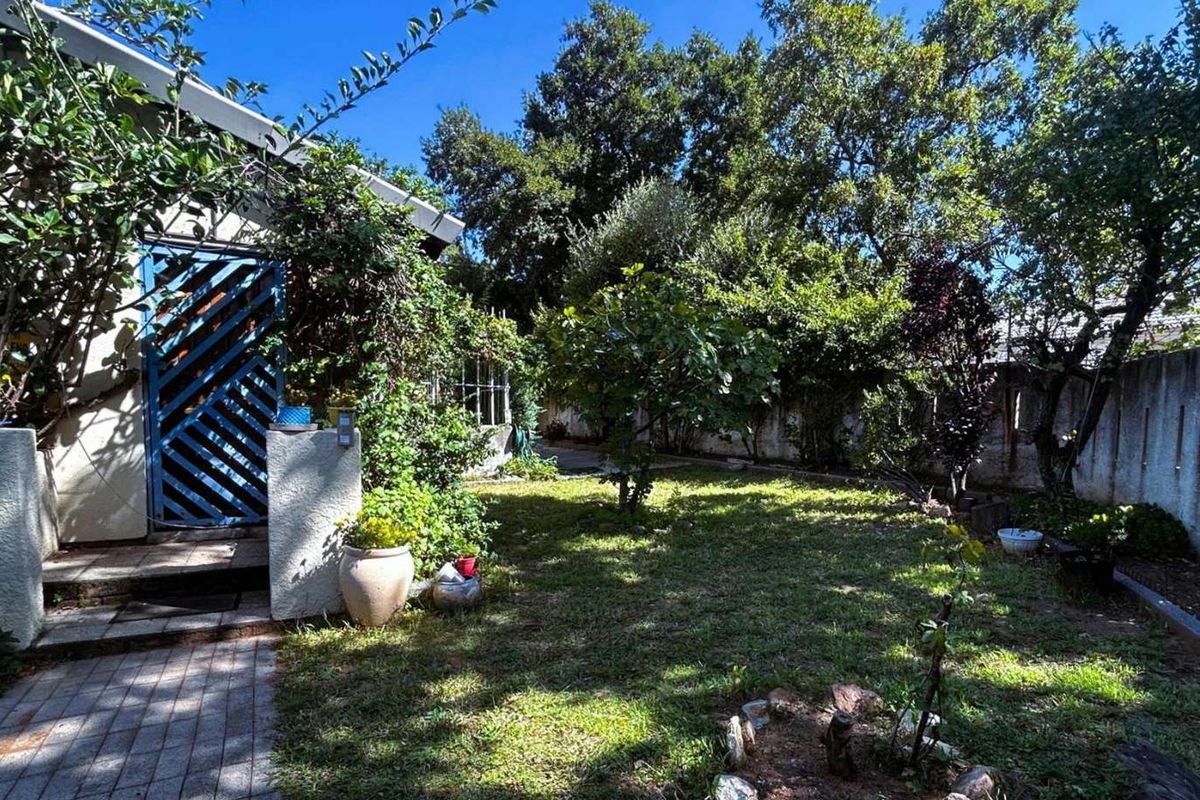 A private rear garden featuring a paved walkway, established trees, and a boundary wall, offering a quiet outdoor space.