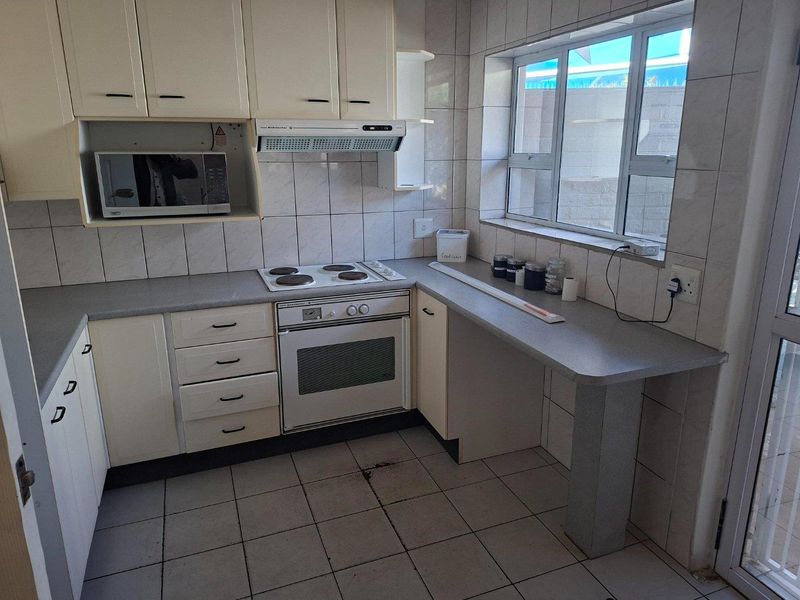 A functional kitchen featuring built-in cabinetry, an electric hob, oven, extractor fan, and tiled finishes throughout.