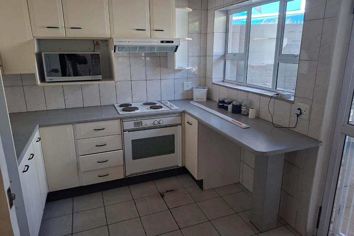 A functional kitchen featuring built-in cabinetry, an electric hob, oven, extractor fan, and tiled finishes throughout.