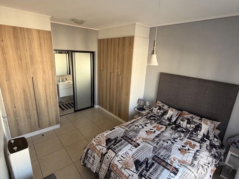 A well-maintained bedroom featuring built-in wooden cupboards, tiled flooring, and an en-suite bathroom with modern vanity.