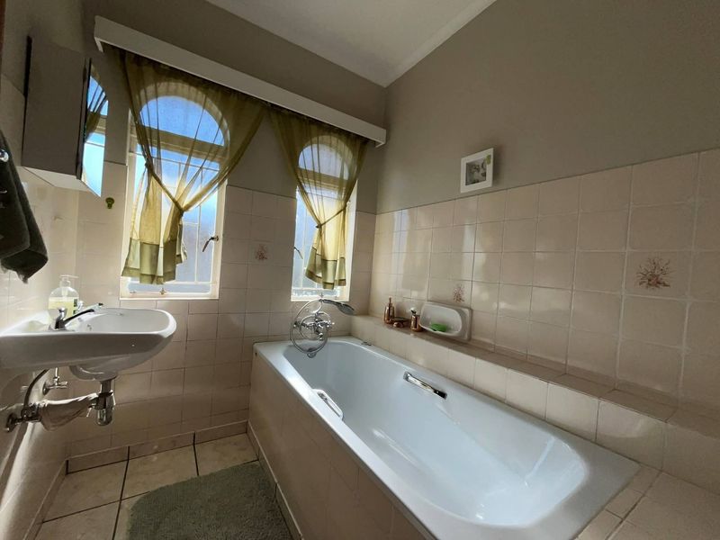 A functional bathroom featuring a built-in bathtub, wall-mounted basin, and classic tiled finishes with natural light from arched windows.