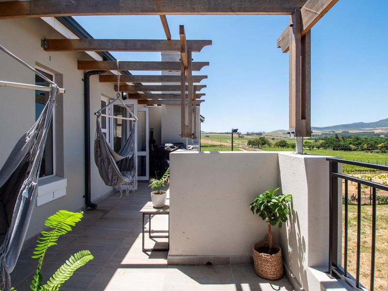 A covered patio area featuring a timber pergola structure, tiled flooring, and a metal balustrade, offering scenic views of the surrounding landscape.