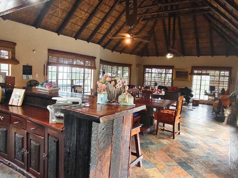 Spacious open-plan living and kitchen area featuring a high thatched ceiling with exposed timber trusses, slate flooring, and rustic timber cabinetry.