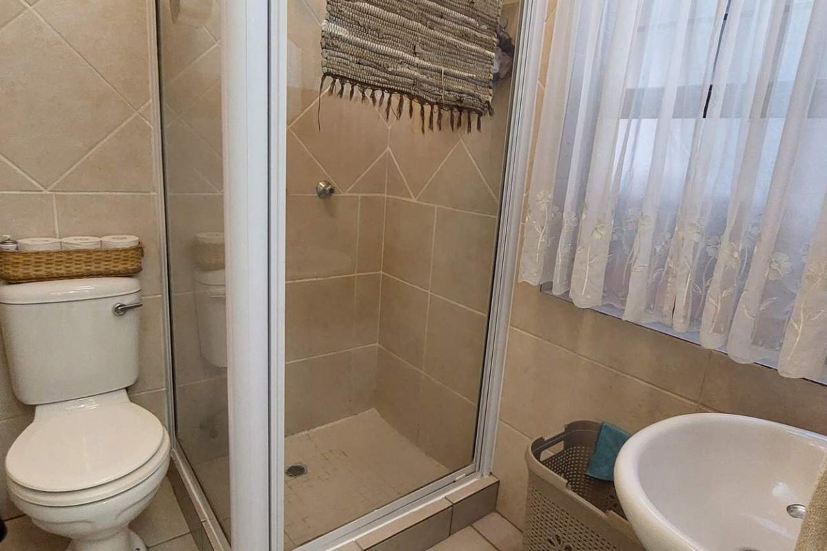 A compact bathroom featuring a tiled shower enclosure, a standard toilet, and a pedestal basin with neutral wall and floor tiling.