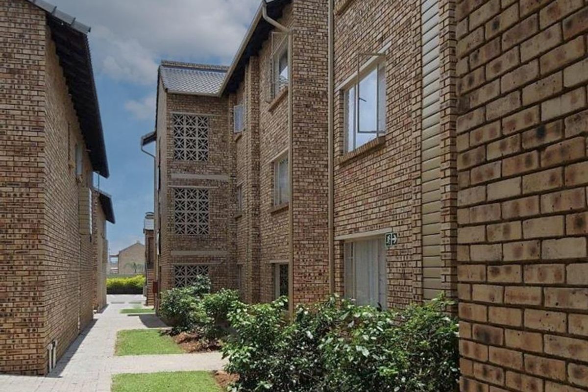 Exterior view of a multi-story apartment complex featuring face brick construction, paved walkways, and landscaped garden areas between the building blocks.