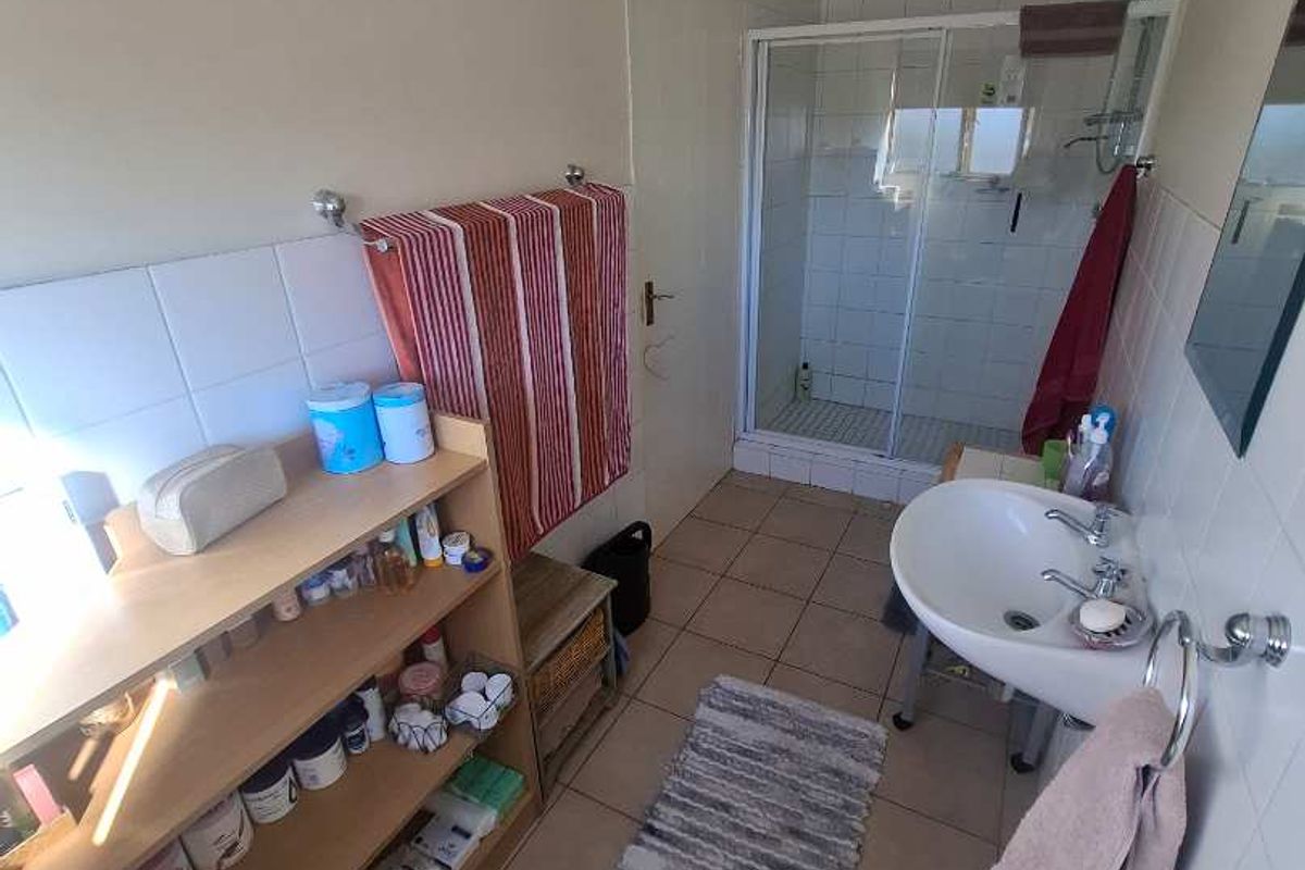 A functional bathroom featuring a tiled shower enclosure, pedestal basin, and toilet with neutral wall finishes and ceramic floor tiling.