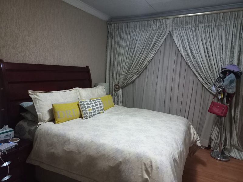 A bedroom featuring laminate flooring, ceiling cornicing, and floor-to-ceiling curtains.