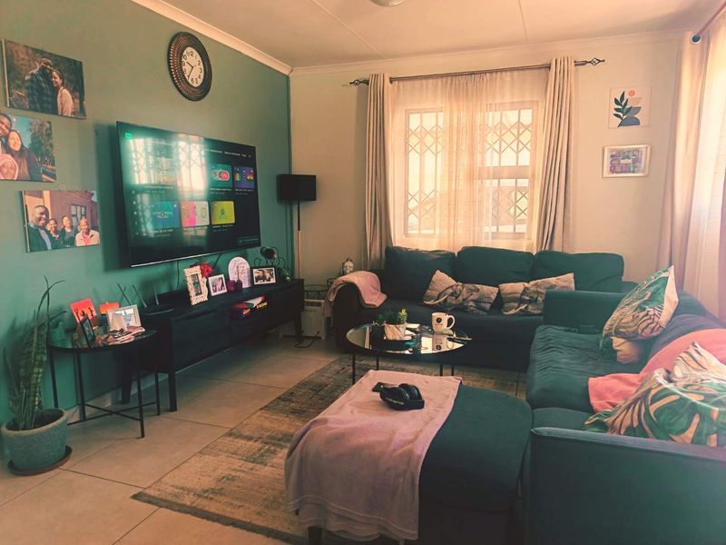 A comfortable living room featuring tiled flooring, security burglar bars on the window, and a feature wall.