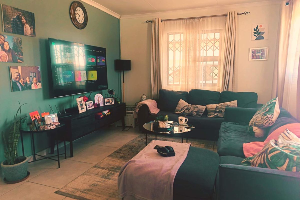 A comfortable living room featuring tiled flooring, security burglar bars on the window, and a feature wall.