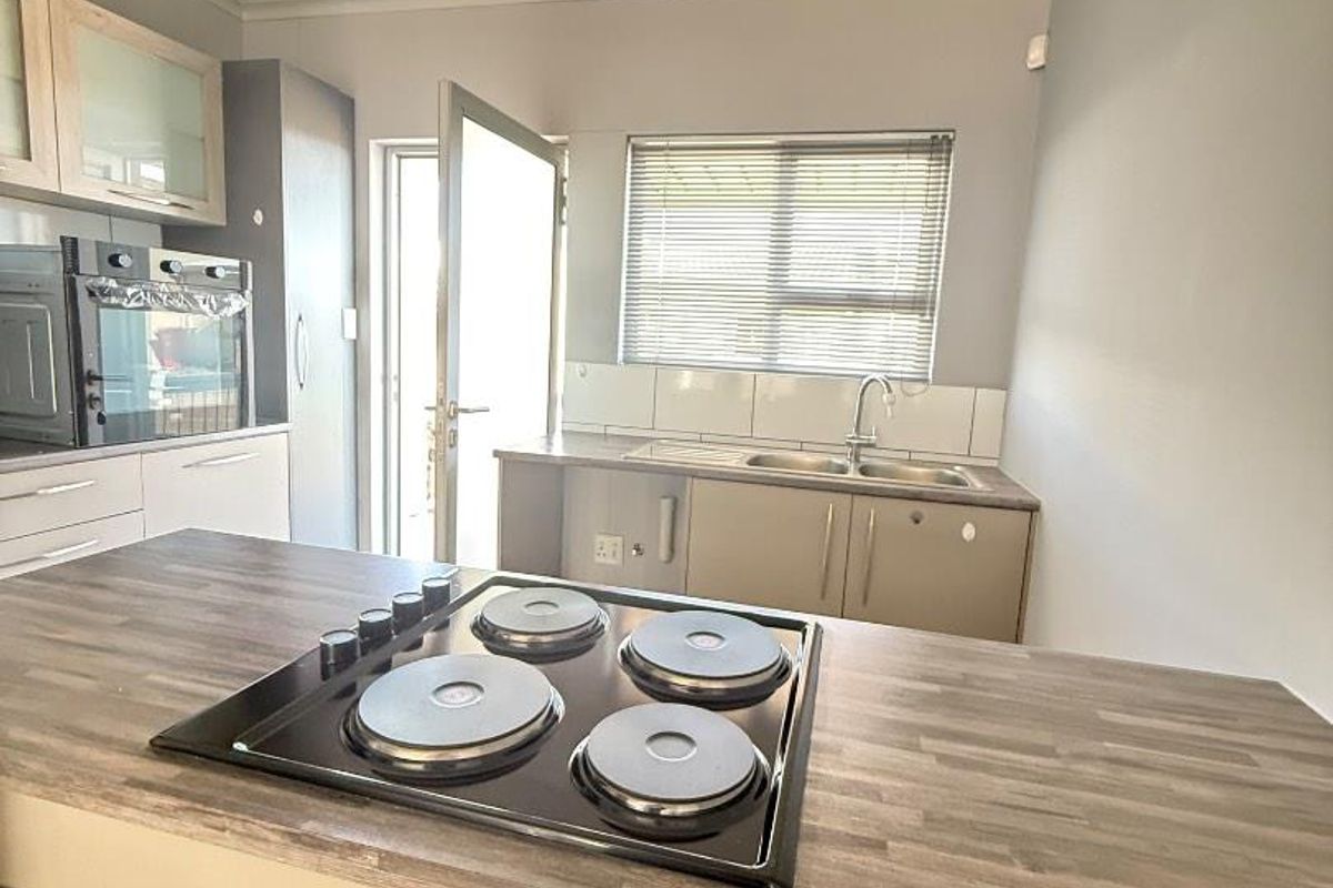 A functional kitchen featuring a built-in electric hob on a wood-look island, integrated oven, double sink, and direct access to the exterior.