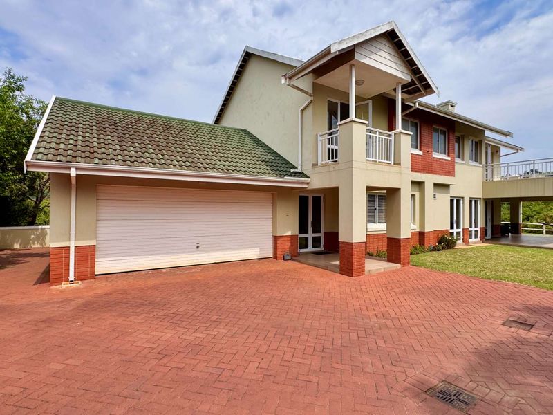 A well-maintained double-storey house featuring a paved driveway, double garage, and an upper-level balcony, set within a neat residential property.