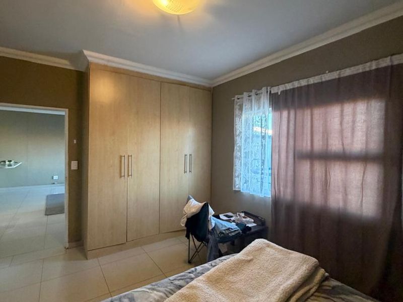 A bedroom featuring built-in cupboards, tiled flooring, and a ceiling light fixture, offering a functional space with neutral wall tones.
