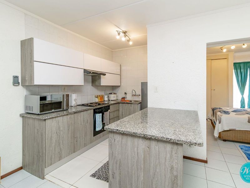 Modern kitchen featuring granite countertops, wood-look cabinetry, built-in oven and hob, and a functional island, with tiled flooring throughout.