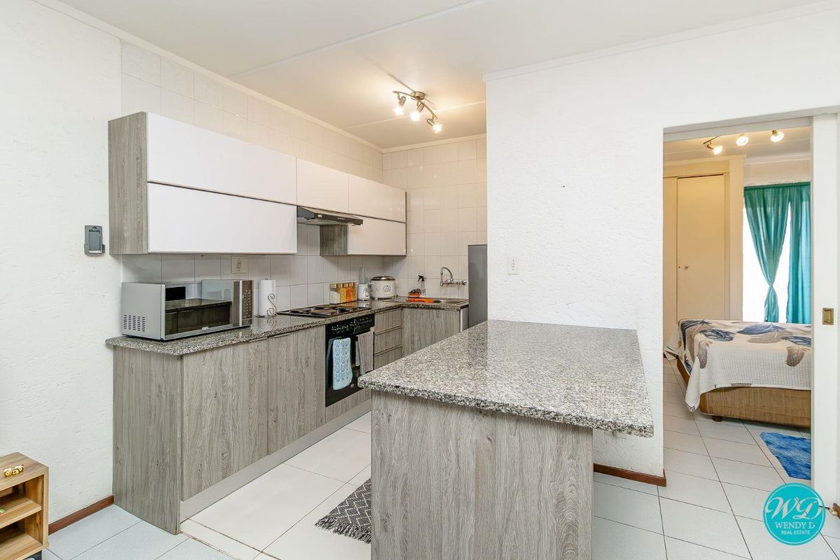 Modern kitchen featuring granite countertops, wood-look cabinetry, built-in oven and hob, and a functional island, with tiled flooring throughout.