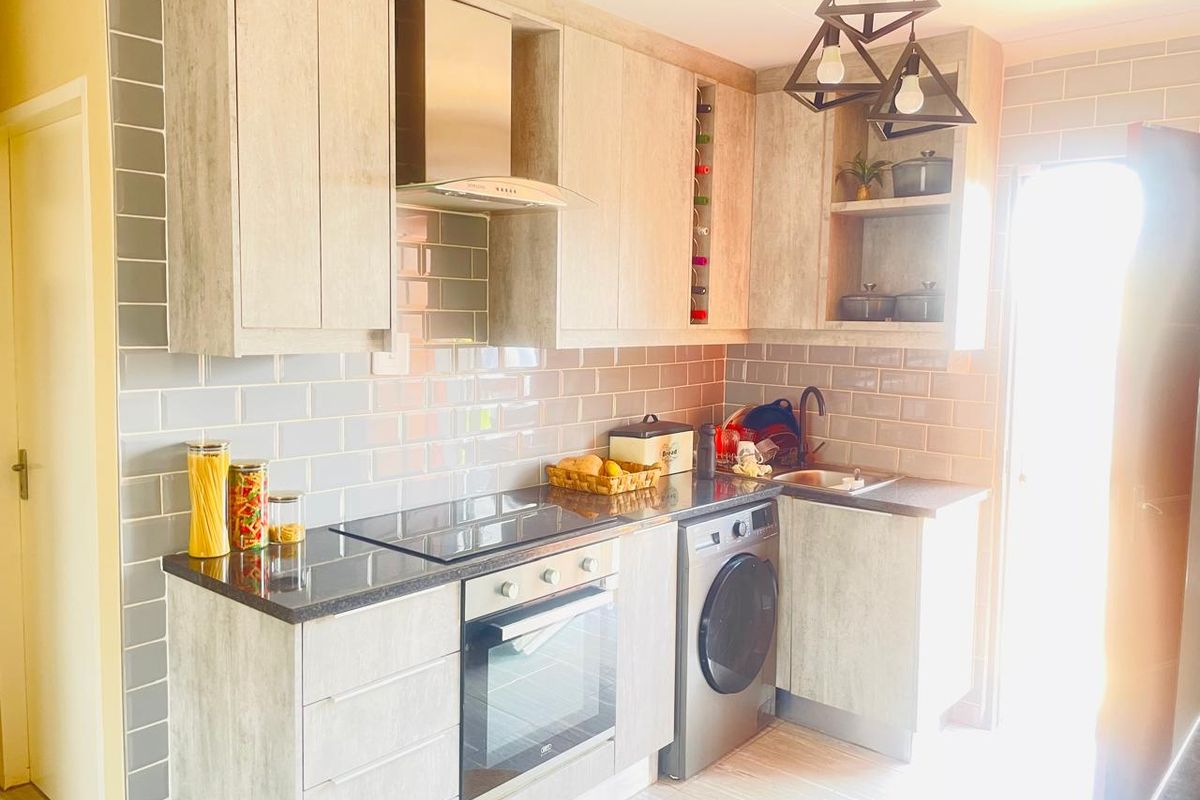 Modern kitchen featuring light wood-grain cabinetry, subway tile backsplash, integrated oven, hob, extractor fan, and a built-in washing machine.