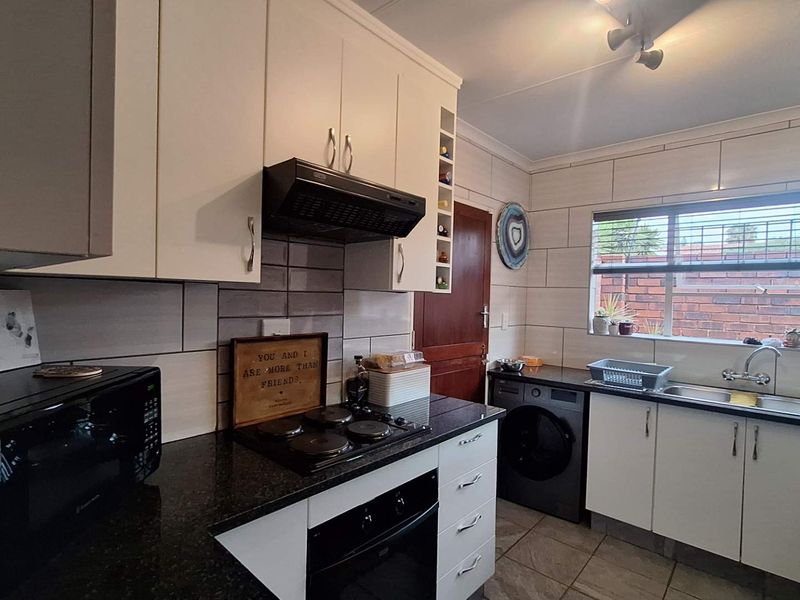 A functional kitchen featuring white cabinetry, dark granite countertops, a built-in oven and hob, and a tiled backsplash with a window overlooking the exterior.