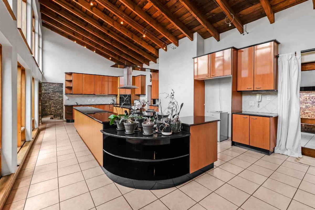 Spacious kitchen featuring high vaulted timber ceilings, extensive wooden cabinetry, a large central island with black stone countertops, and tiled flooring.