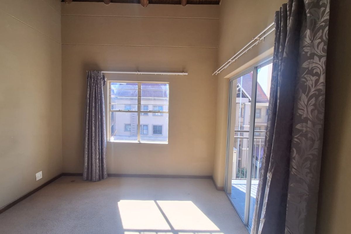 A spacious, empty bedroom featuring high ceilings, carpeted flooring, a large window, and sliding glass doors leading to a private balcony.
