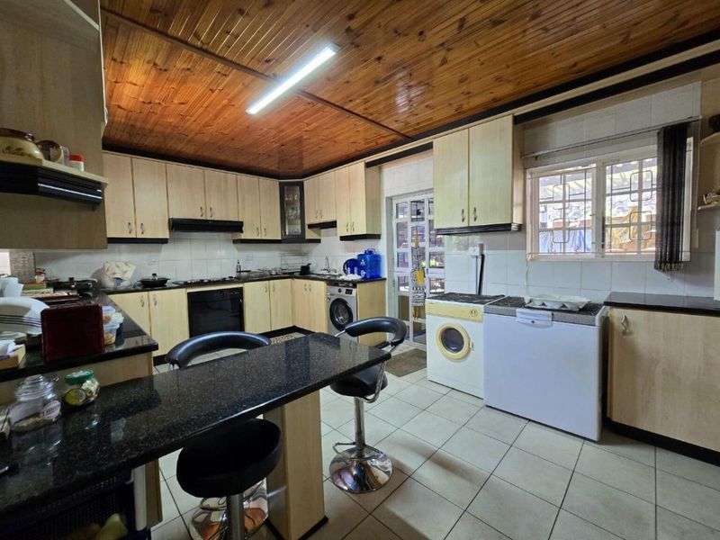 Functional kitchen featuring granite countertops, built-in cabinetry, integrated oven and hob, tiled flooring, and a distinctive timber ceiling.