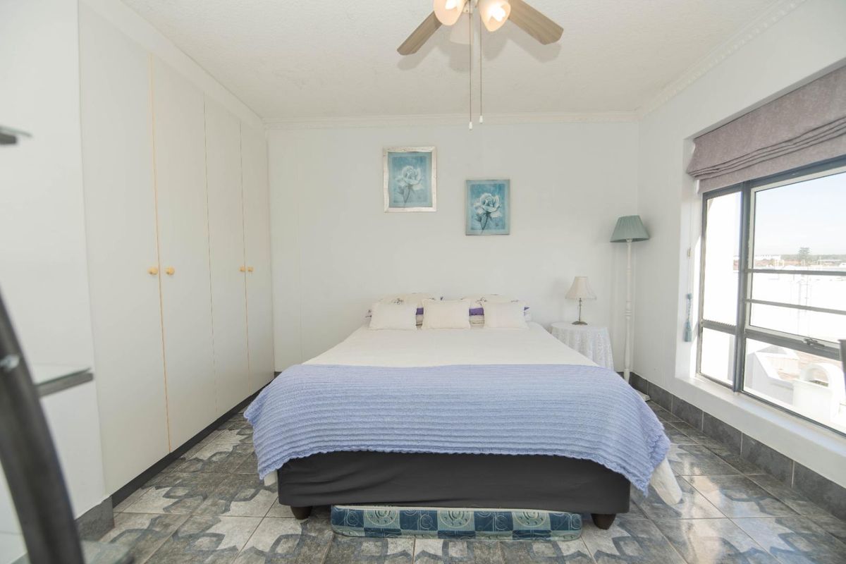 A bedroom featuring built-in cupboards, tiled flooring, and a ceiling fan, offering a functional space with natural light.