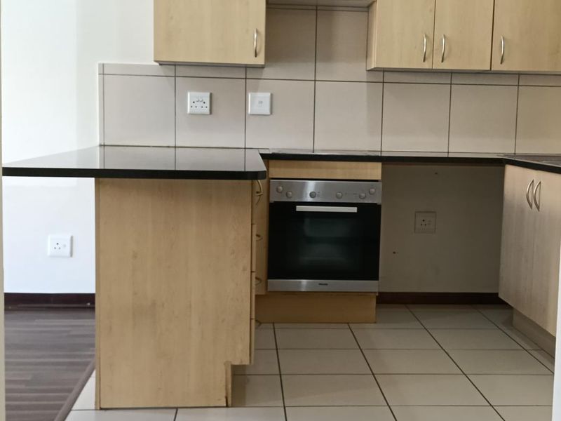 A functional kitchen featuring light wood-finish cabinetry, dark countertops, a built-in oven, and neutral tiled flooring and backsplash.