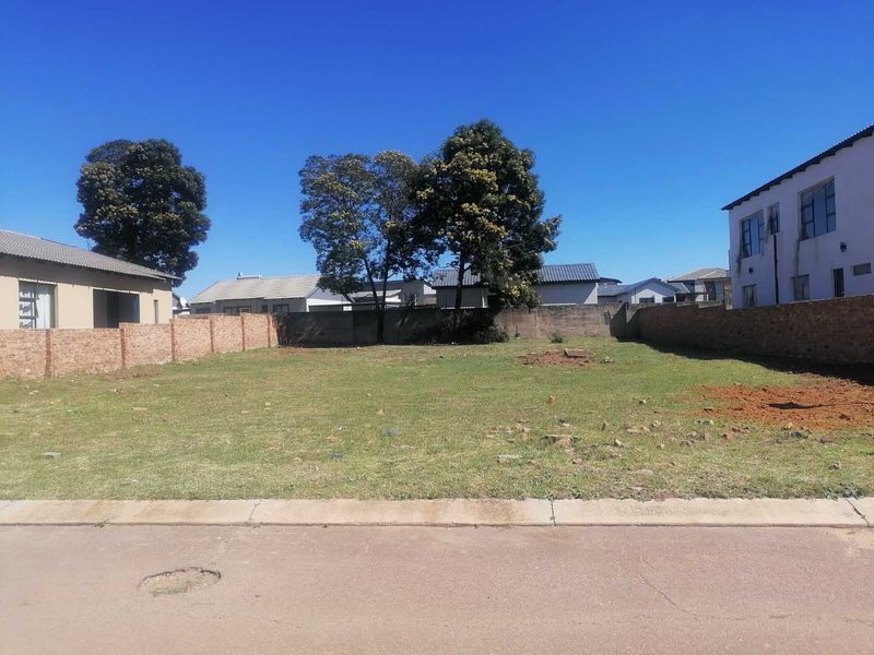 A vacant residential plot featuring a level grass surface, enclosed by perimeter brick walls, situated along a paved street.