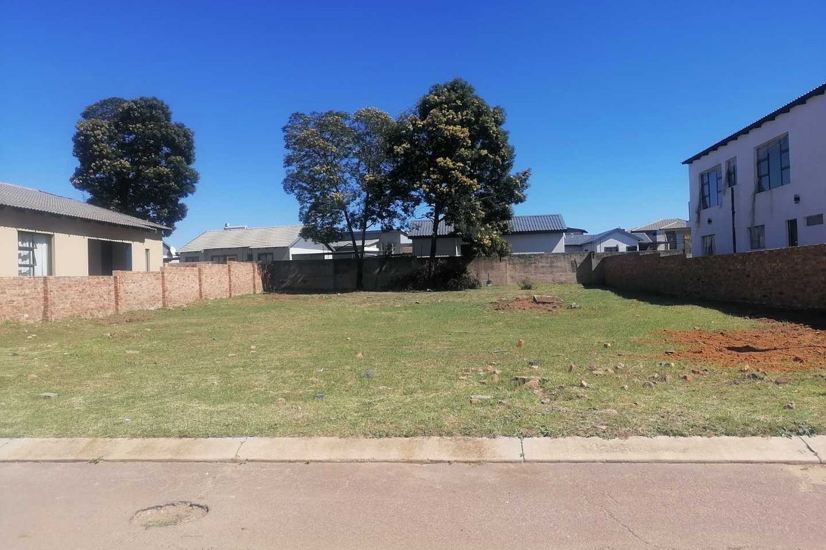 A vacant residential plot featuring a level grass surface, enclosed by perimeter brick walls, situated along a paved street.