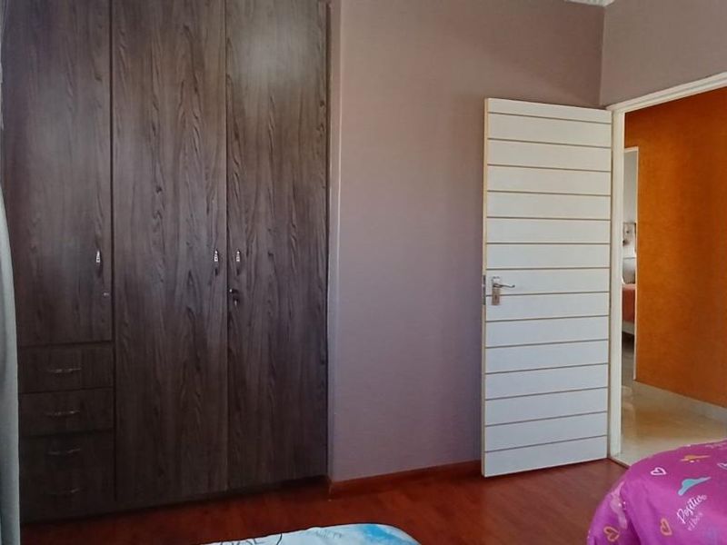 A bedroom featuring dark wood-finish built-in wardrobes, laminate flooring, and a modern horizontal slatted interior door.