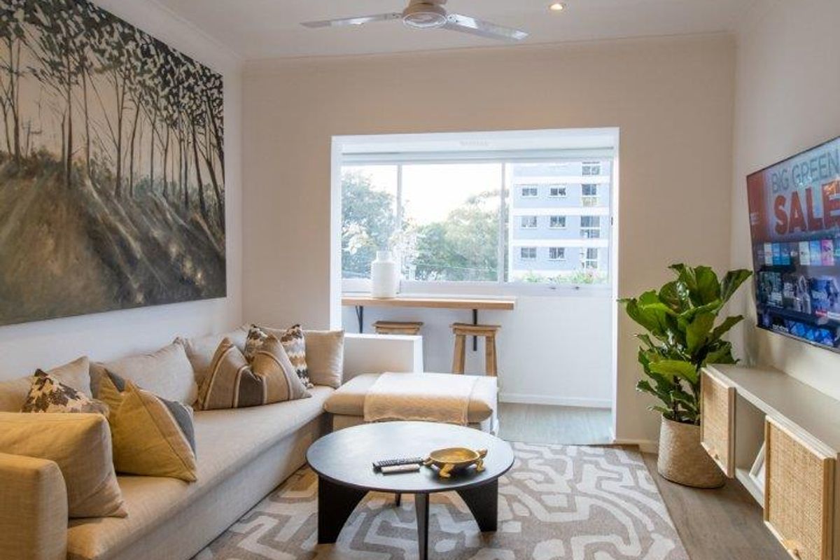 A well-lit living room featuring recessed downlights, a ceiling fan, and large windows providing natural light and a view of the surrounding area.