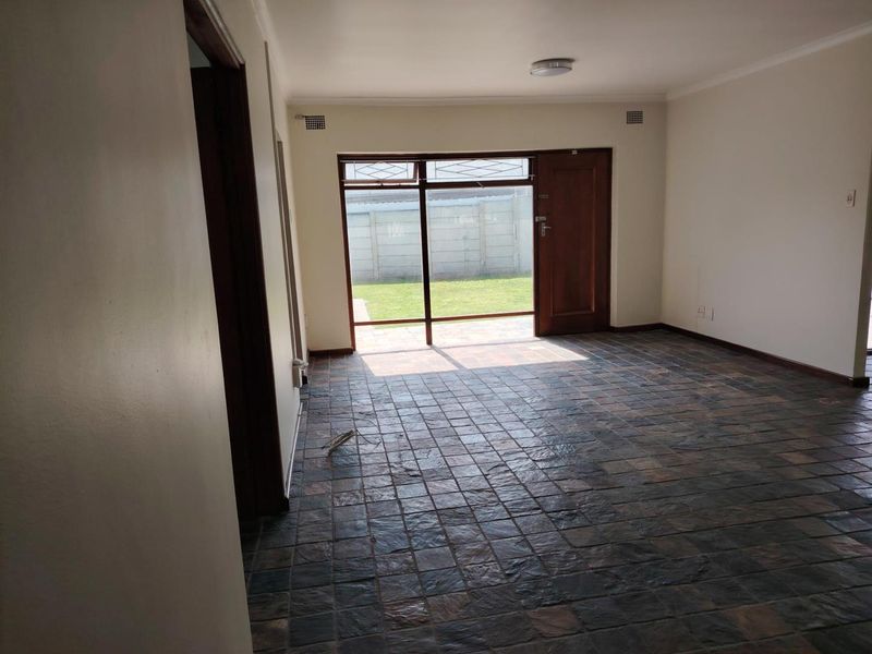 An empty living room featuring slate tile flooring and a large sliding glass door providing direct access to the rear garden.