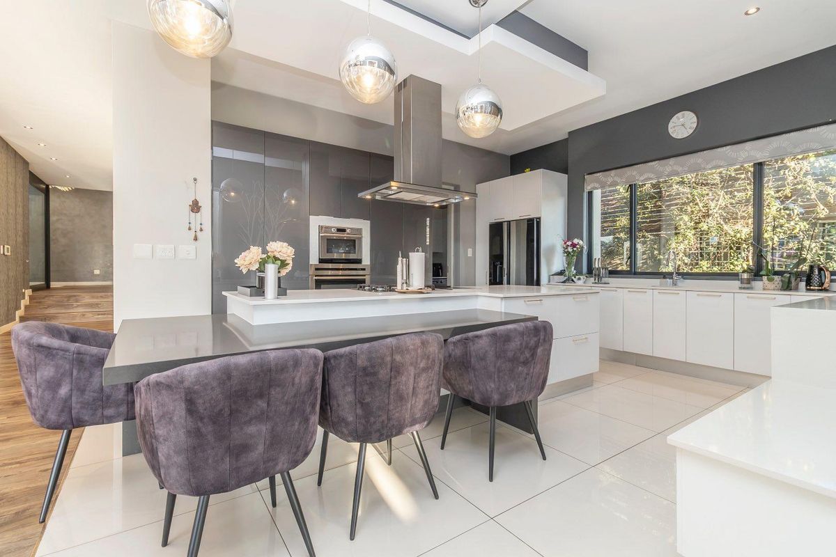 Modern kitchen featuring a central island with breakfast bar, high-gloss cabinetry, built-in oven, extractor fan, and sleek stone countertops with recessed lighting.