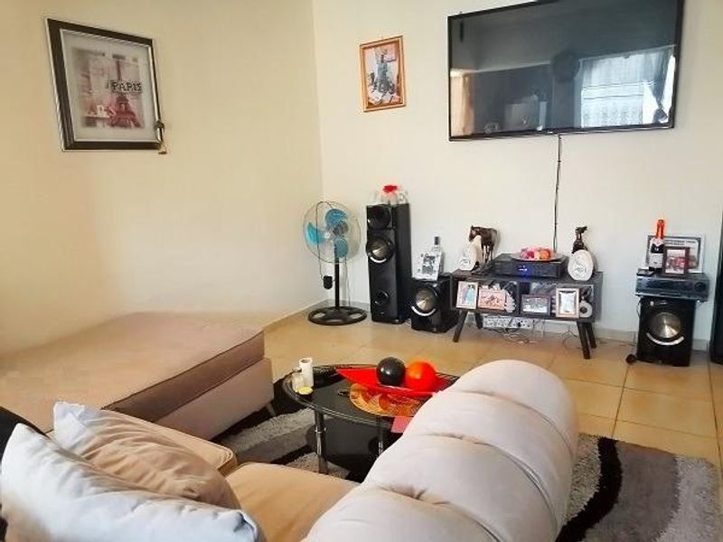 A living room featuring tiled flooring and a wall-mounted television, providing a functional space for relaxation and entertainment.