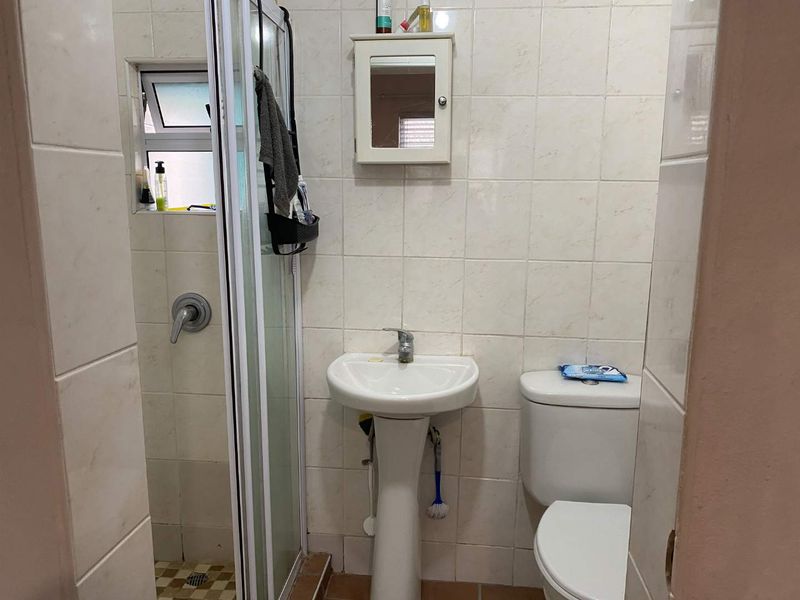 Compact bathroom featuring a pedestal sink, toilet, and a glass-enclosed shower with tiled walls and flooring.