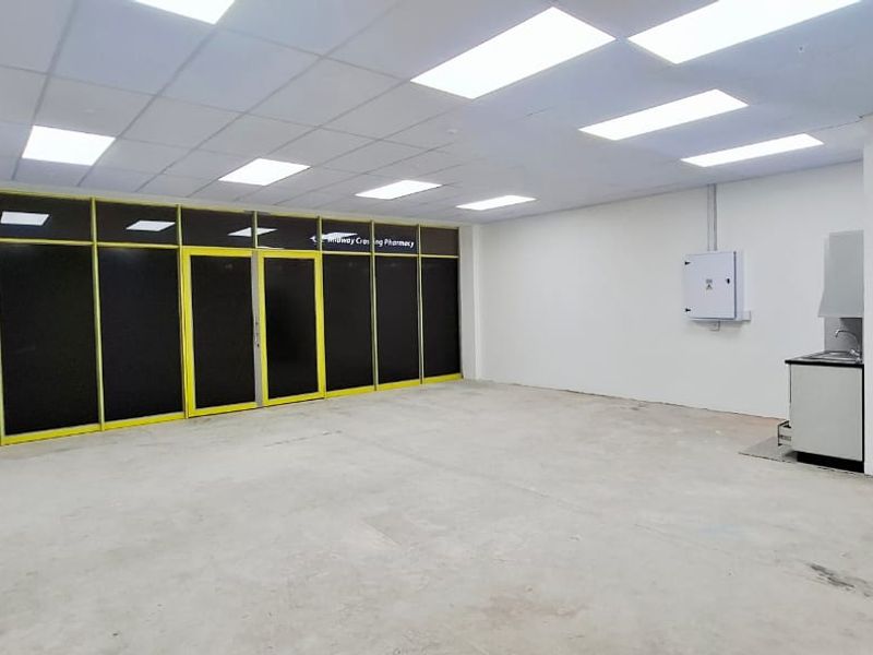 An open-plan commercial space featuring a suspended ceiling, recessed lighting, an aluminium shopfront, and a small kitchenette area with a sink.