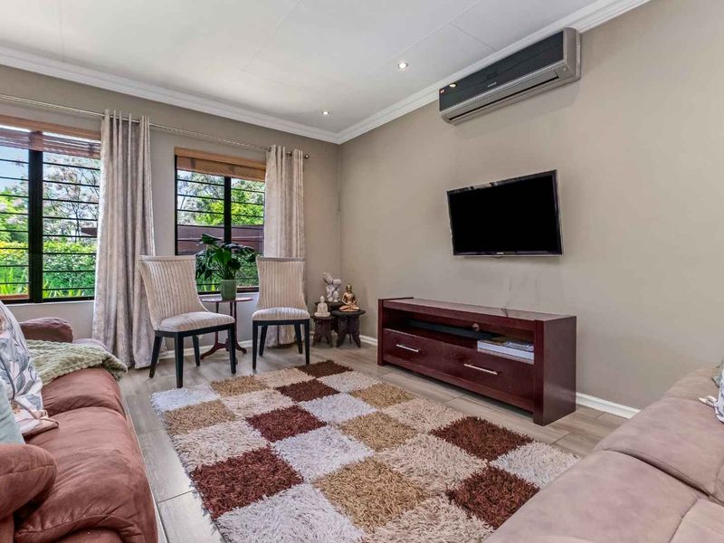 A well-maintained living room featuring tiled flooring, coved ceilings with recessed lighting, and a wall-mounted split-system air conditioner.