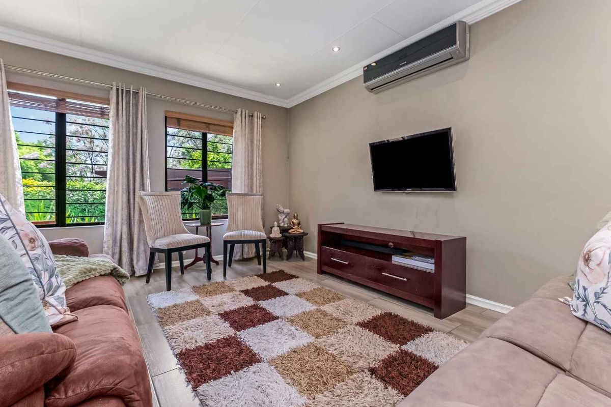 A well-maintained living room featuring tiled flooring, coved ceilings with recessed lighting, and a wall-mounted split-system air conditioner.