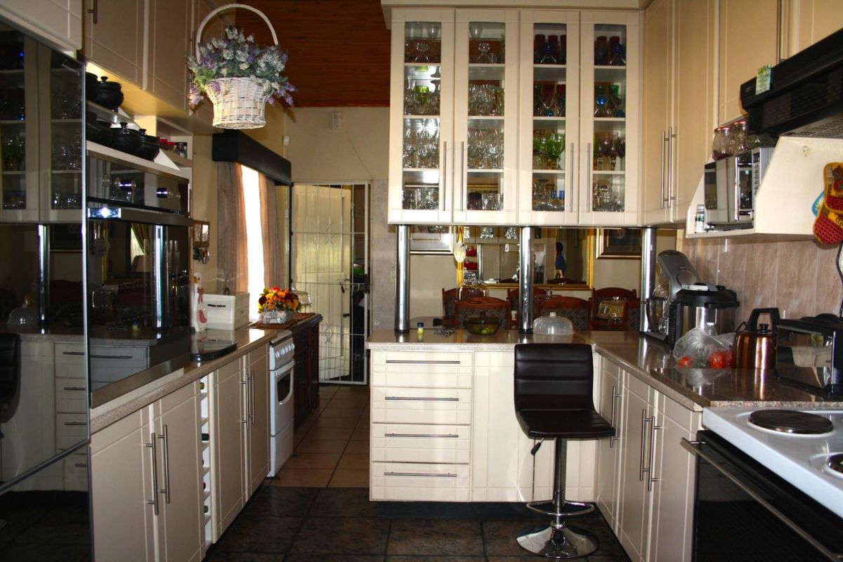 A functional kitchen featuring cream-colored cabinetry, granite countertops, built-in oven, and glass-fronted display cabinets, with tiled flooring throughout.
