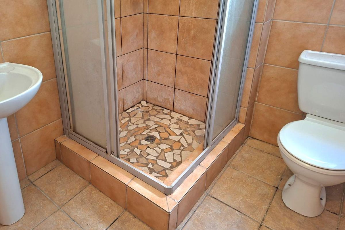 A dated bathroom featuring a pedestal basin, a corner shower enclosure with tiled base, and a standard toilet with ceramic wall and floor tiling.