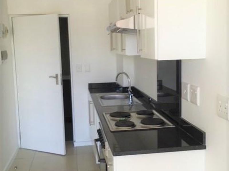 A clean, compact kitchen featuring white cabinetry, black granite countertops, integrated electric hob, oven, and extractor fan with neutral tiled flooring.