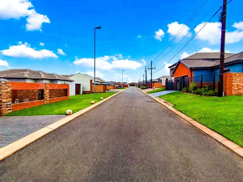 A clear street view of a well-maintained residential estate featuring paved roads, manicured lawns, and established brick boundary walls.