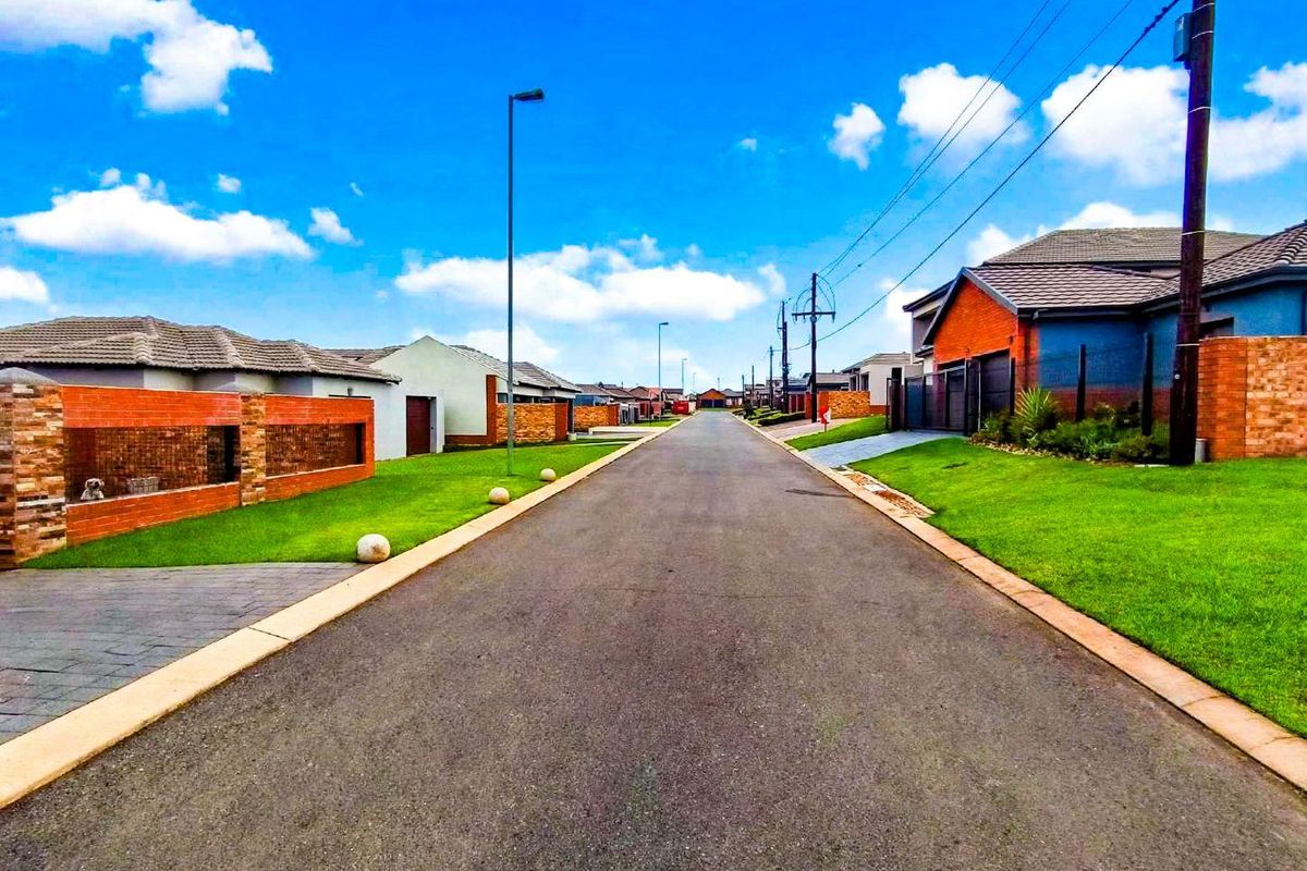 A clear street view of a well-maintained residential estate featuring paved roads, manicured lawns, and established brick boundary walls.